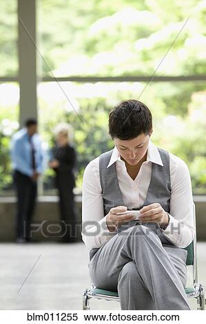 Stock Photography - Caucasian businesswoman text messaging in lobby. Fotosearch
