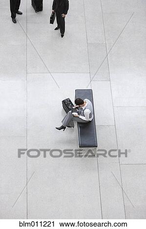 Stock Image - Caucasian businesswoman with suitcase sitting in lobby. Fotosearch