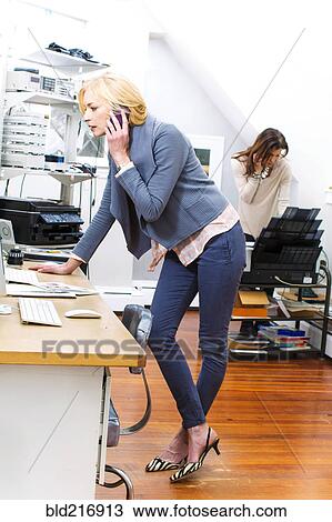 Stock Image - Caucasian businesswomen talking on cell phones in office. Fotosearch