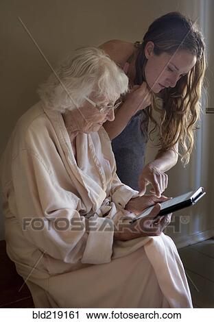 Stock Image - Caucasian caregiver helping older woman use digital tablet. Fotosearch