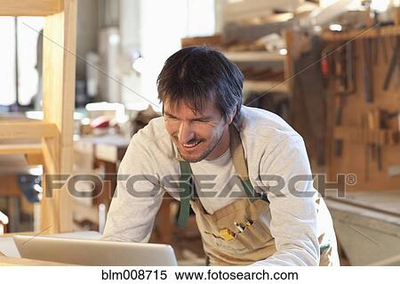 Stock Photography - Caucasian carpenter using laptop in workshop. Fotosearch