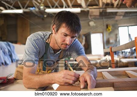 Stock Image - Caucasian carpenter working in workshop. Fotosearch
