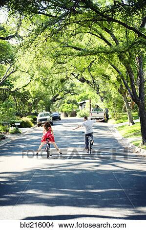 Picture - Caucasian children riding bicycles on suburban neighborhood street. Fotosearch