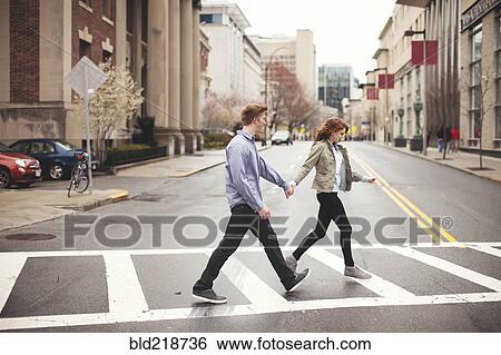 Stock Photograph - Caucasian couple holding hands crossing city intersection. Fotosearch