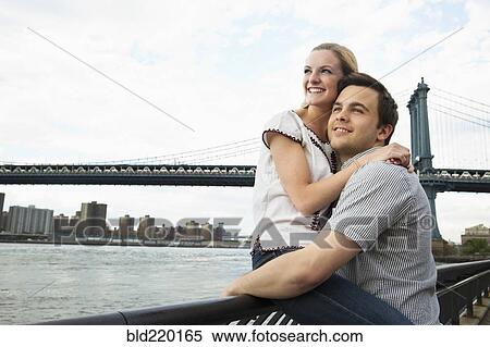 Stock Photography - Caucasian couple hugging under Brooklyn Bridge, Brooklyn, New York, United States. Fotosearch