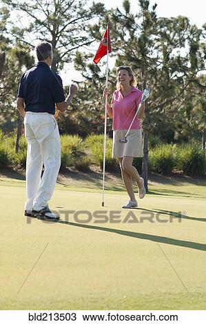 Stock Image - Caucasian couple playing golf on course. Fotosearch