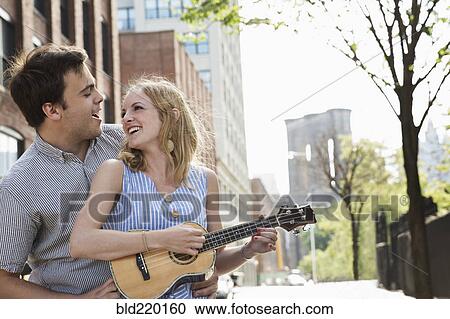 Stock Image - Caucasian couple playing ukulele in city. Fotosearch