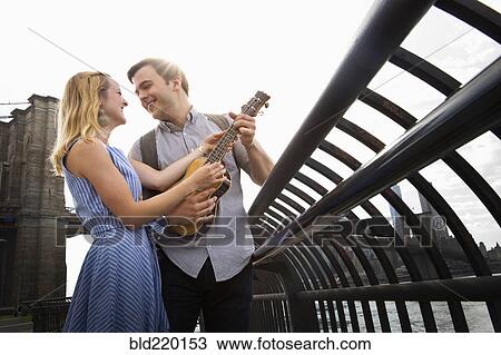 Stock Image - Caucasian couple playing ukulele on urban waterfront. Fotosearch