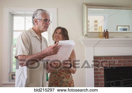 Stock Photo - Caucasian couple reading paper in living room. Fotosearch