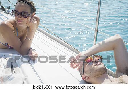 Stock Image - Caucasian couple sunbathing on boat deck. Fotosearch