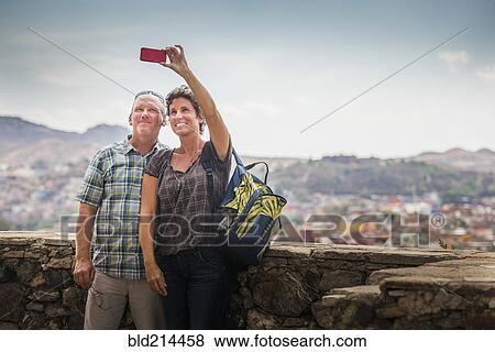 Stock Photo - Caucasian couple taking cell phone photograph together on rooftop. Fotosearch