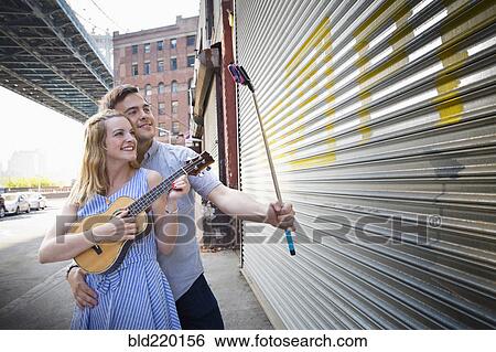 Stock Photograph - Caucasian couple taking selfie and playing ukulele in city. Fotosearch