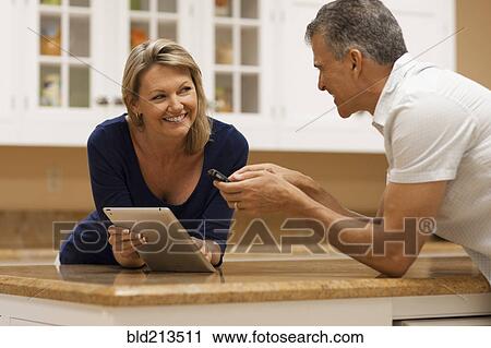 Caucasian couple using digital tablet and cell phone at kitchen counter View Large Photo Image Stock Image - Caucasian couple using digital tablet and cell phone at kitchen counter. Fotosearch