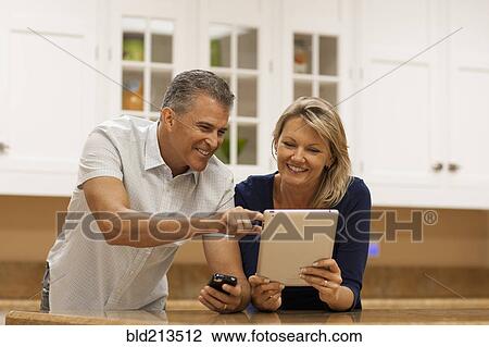 Caucasian couple using digital tablet and cell phone at kitchen counter View Large Photo Image Stock Image - Caucasian couple using digital tablet and cell phone at kitchen counter. Fotosearch