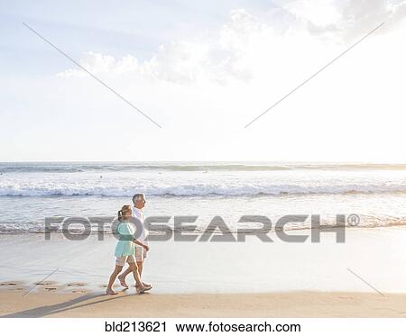 Stock Image - Caucasian couple walking on beach. Fotosearch