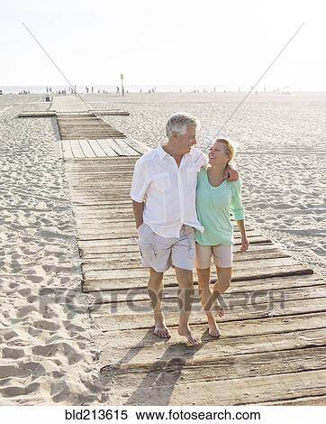 Stock Photography - Caucasian couple walking on wooden boardwalk on beach. Fotosearch