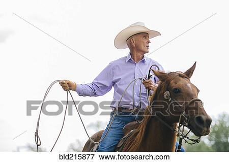 Stock Photo - Caucasian cowboy riding horse in rodeo. Fotosearch