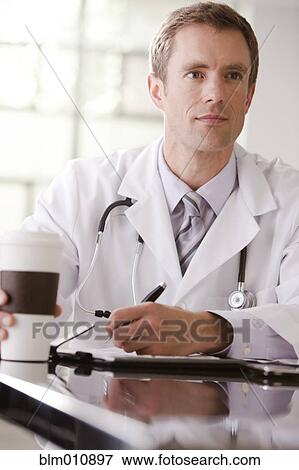 Stock Photo - Caucasian doctor drinking coffee and writing in medical record. Fotosearch