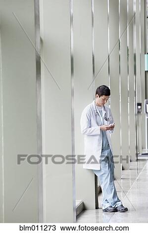 Stock Image - Caucasian doctor text messaging in lobby. Fotosearch