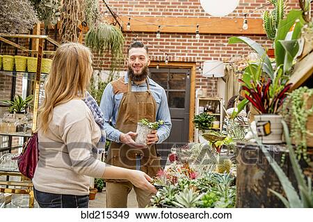 Stock Photo - Caucasian employee helping customer in plant nursery. Fotosearch