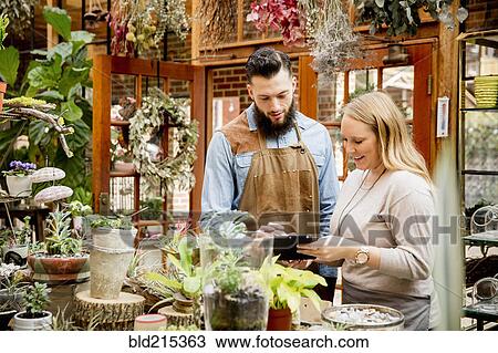 Stock Image - Caucasian employees using digital tablet in plant nursery. Fotosearch