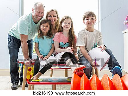 Stock Image - Caucasian family smiling at table in playroom. Fotosearch