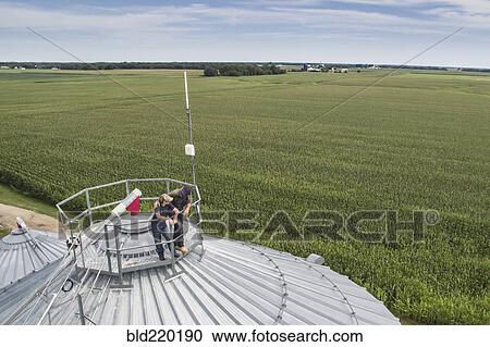 Stock Image - Caucasian farmer and son admiring farm from silo. Fotosearch