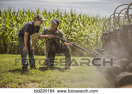 Picture - Caucasian farmer and son cleaning machinery on farm. Fotosearch