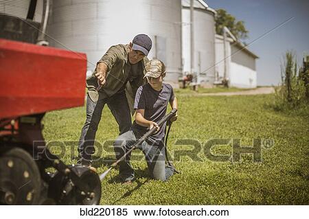 Stock Photography - Caucasian farmer and son cleaning machinery on farm. Fotosearch