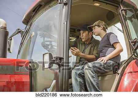 Stock Photograph - Caucasian farmer teaching son to drive tractor. Fotosearch