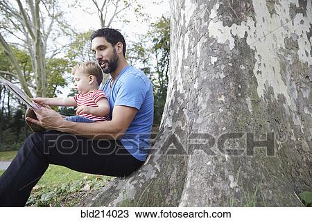 Stock Image - Caucasian father and baby son using digital tablet outdoors. Fotosearch