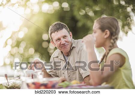 Stock Image - Caucasian father and daughter eating in backyard. Fotosearch