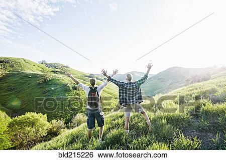 Stock Photograph - Caucasian father and son cheering on grassy hillside. Fotosearch