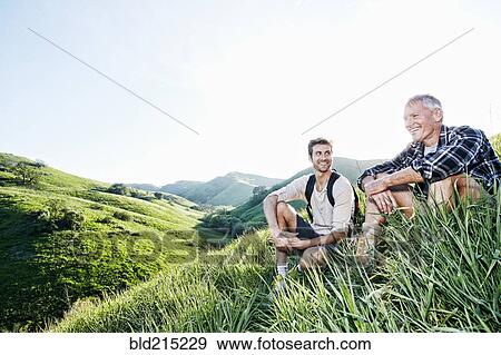 Stock Photo - Caucasian father and son sitting on grassy hillside. Fotosearch