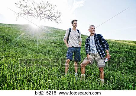 Stock Photo - Caucasian father and son standing on grassy hillside. Fotosearch