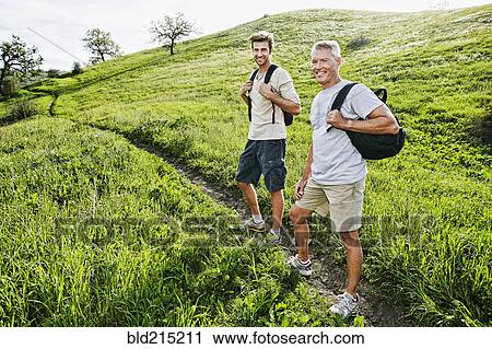 Stock Image - Caucasian father and son walking on dirt path. Fotosearch