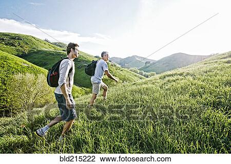 Stock Image - Caucasian father and son walking on grassy hillside. Fotosearch