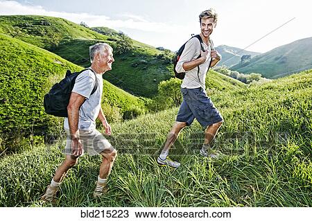Stock Image - Caucasian father and son walking on grassy hillside. Fotosearch