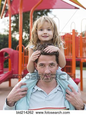 Stock Image - Caucasian father holding daughter at playground. Fotosearch