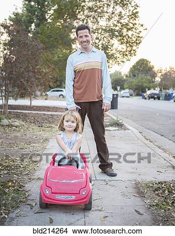 Picture - Caucasian father pushing daughter in toy car. Fotosearch