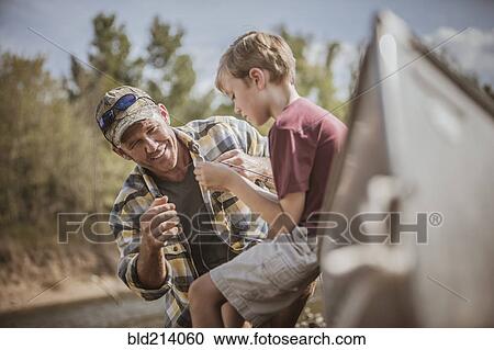 Stock Image - Caucasian father teaching son to tie fishing lures. Fotosearch