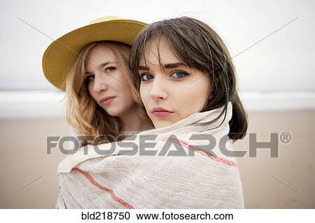 Stock Image - Caucasian friends wrapped in blanket on beach. Fotosearch