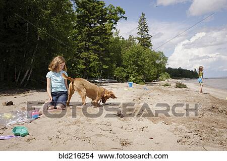 Picture - Caucasian girl and puppy playing on beach. Fotosearch