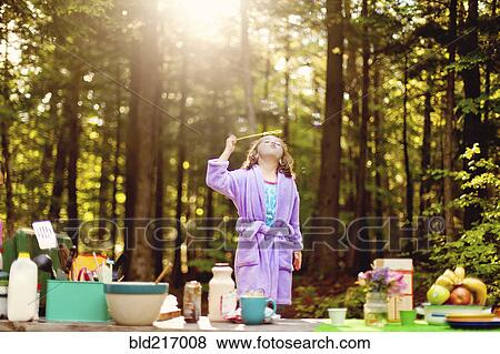 Stock Photo - Caucasian girl blowing bubbles in forest. Fotosearch