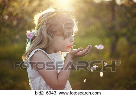 Stock Image - Caucasian girl blowing flower petals outdoors. Fotosearch