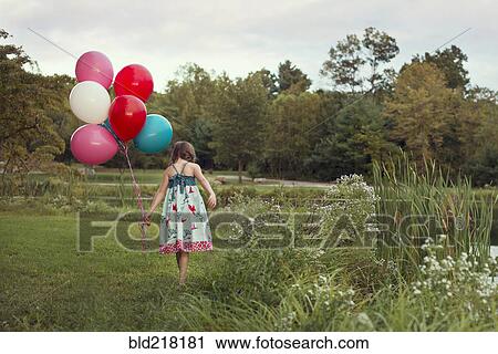 Stock Image - Caucasian girl carrying balloons in rural field. Fotosearch