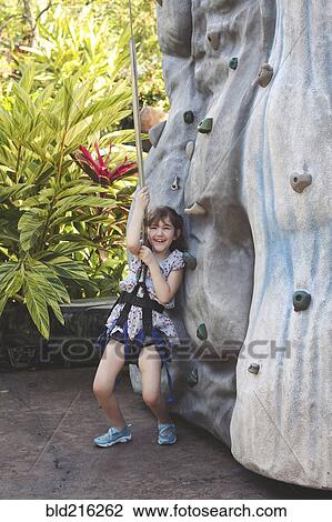Stock Image - Caucasian girl climbing rock wall in harness. Fotosearch