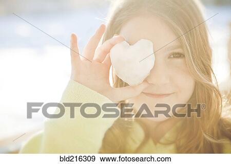 Stock Photo - Caucasian girl covering eye with heart shape. Fotosearch