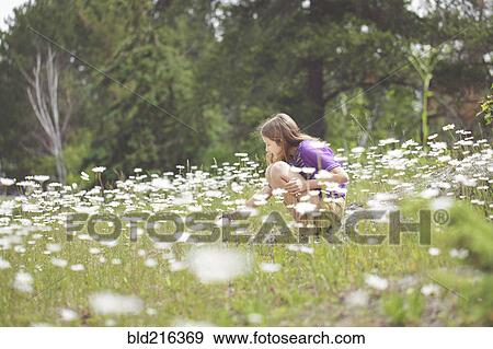 Stock Photo - Caucasian girl crouching in field of flowers. Fotosearch
