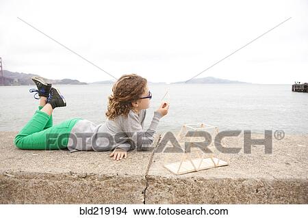 Picture - Caucasian girl examining homework project on wall over ocean. Fotosearch